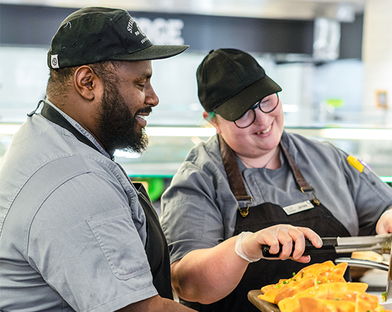 Two employees smiling and serving food